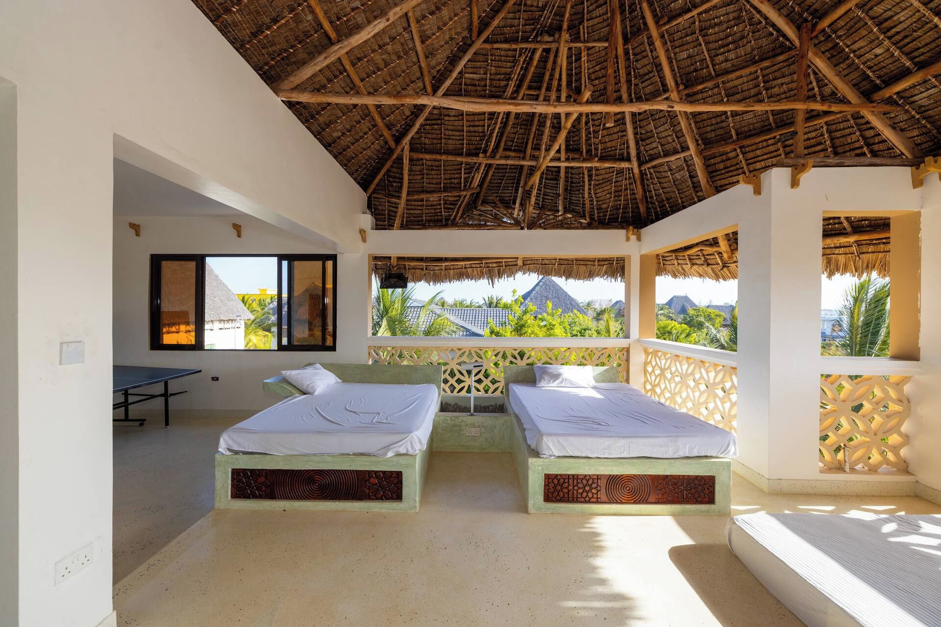 A room with two beds, a table, and a view of a mountain.