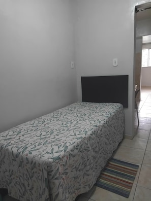 Habitació petita amb un llit individual, un edredó amb motius florals, un panell de fons negre i una catifes a ratlles al sòl.