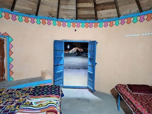 A room with a bed, a small table, and an open door leading outside. - White Rann Homestay (Dhordo)