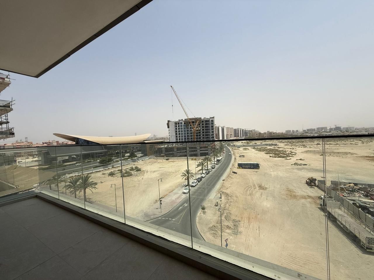 Vista da un grattacielo su un cantiere edile con un grande edificio in costruzione, una strada con auto parcheggiate e un cielo sereno.