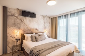 Una habitación de hotel moderna con una cama grande, un televisor de pantalla plana montado en la pared y vistas de la ciudad a través de amplias ventanas.