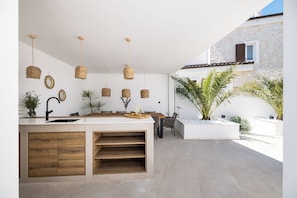 Una cocina moderna con una isla central, lámparas colgantes de mimbre y vistas a un edificio de piedra.