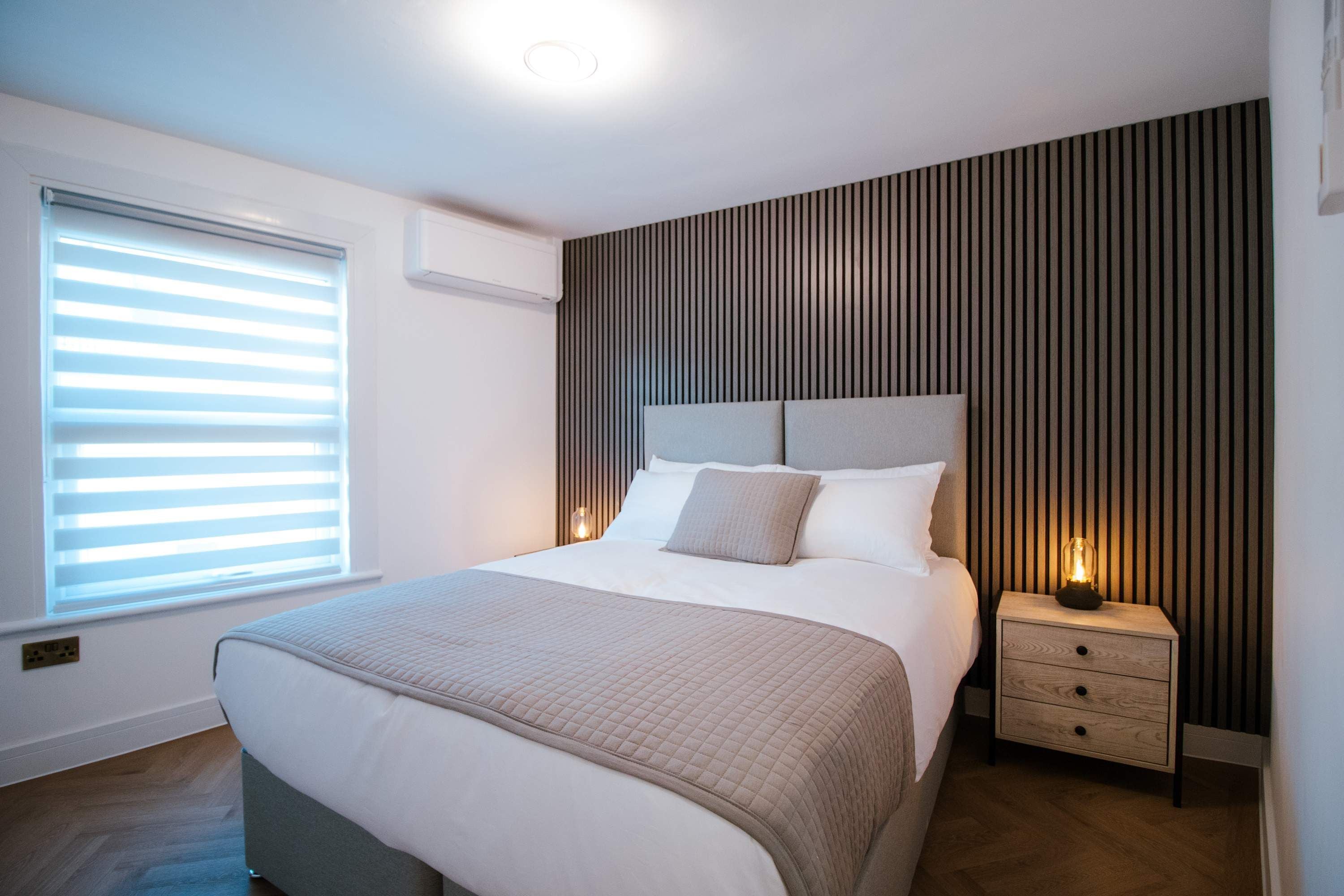 A modern bedroom with a bed, bedside tables, and a window with blinds.