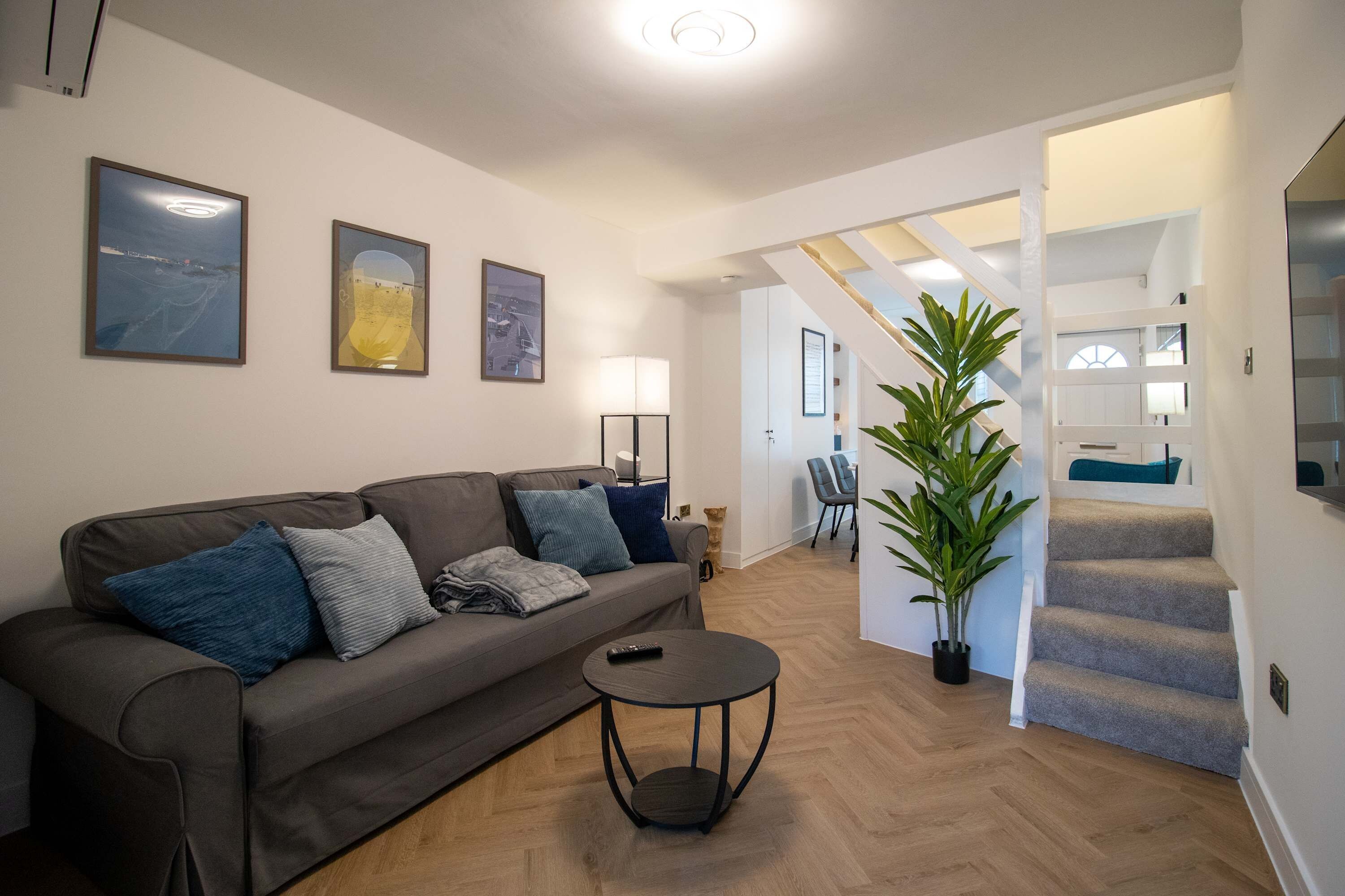 A modern living room with a grey sofa, a small round table, and a staircase leading to another level.