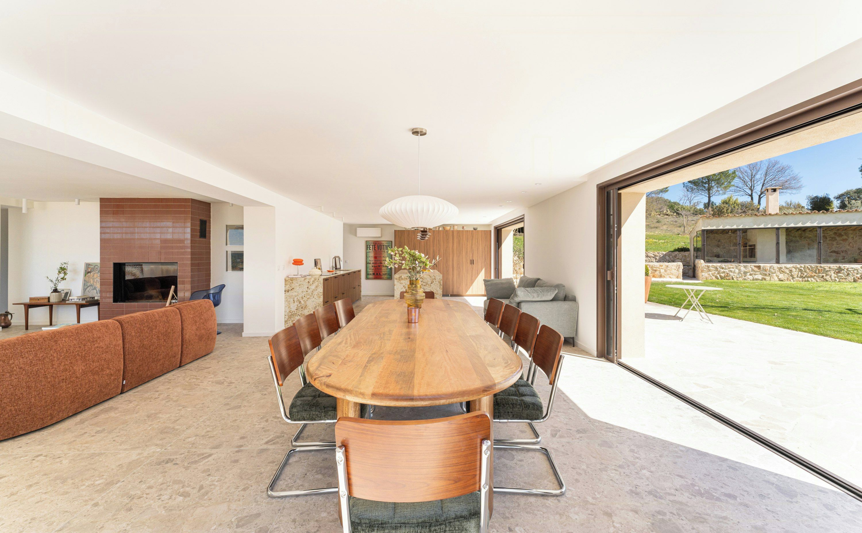 A modern dining area with a large wooden table, comfortable seating, and a view of the outdoors.
