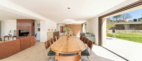 A modern dining area with a large wooden table, comfortable seating, and a view of the outdoors.