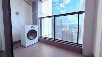 A laundry room with a washing machine, a window with a city view, and a tiled floor.