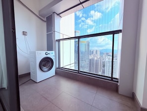 A laundry room with a washing machine, a window with a city view, and a tiled floor. - Dongfeng Shanhai Serviced Apartment (Shenzhen)
