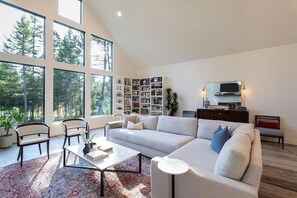 Ein modernes Wohnzimmer mit großem Fenster, einer Couch, einem Couchtisch und einem Bücherregal.