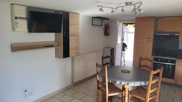 Una cocina compacta con una mesa de comedor, sillas, un televisor integrado y un refrigerador pequeño.