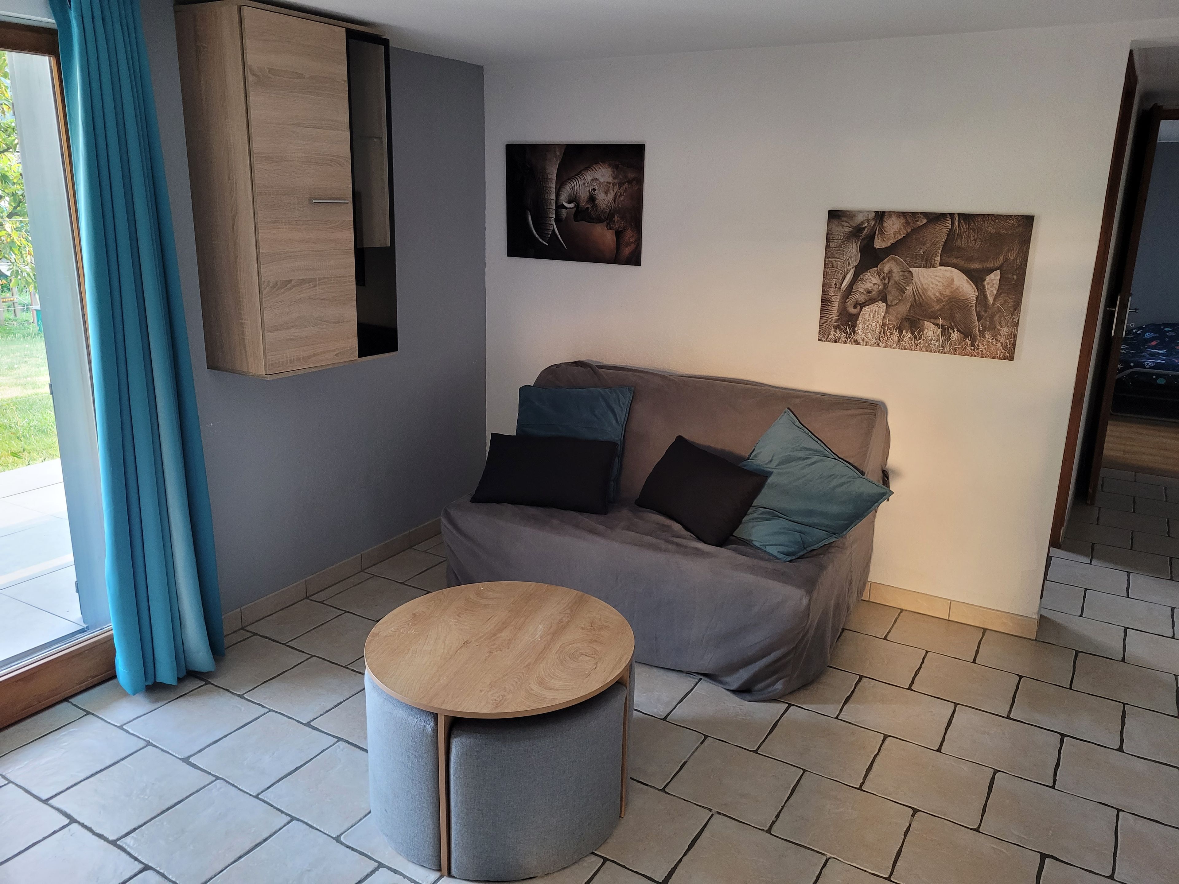 Un salon moderne avec un canapé gris, une table basse ronde en bois et deux tableaux représentant des éléphants, accrochés au mur.