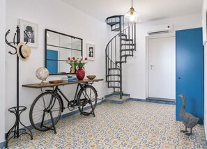 A room with a spiral staircase, a globe, a vase with flowers, and a blue door with a bird decoration. - New Listing (Napoli)