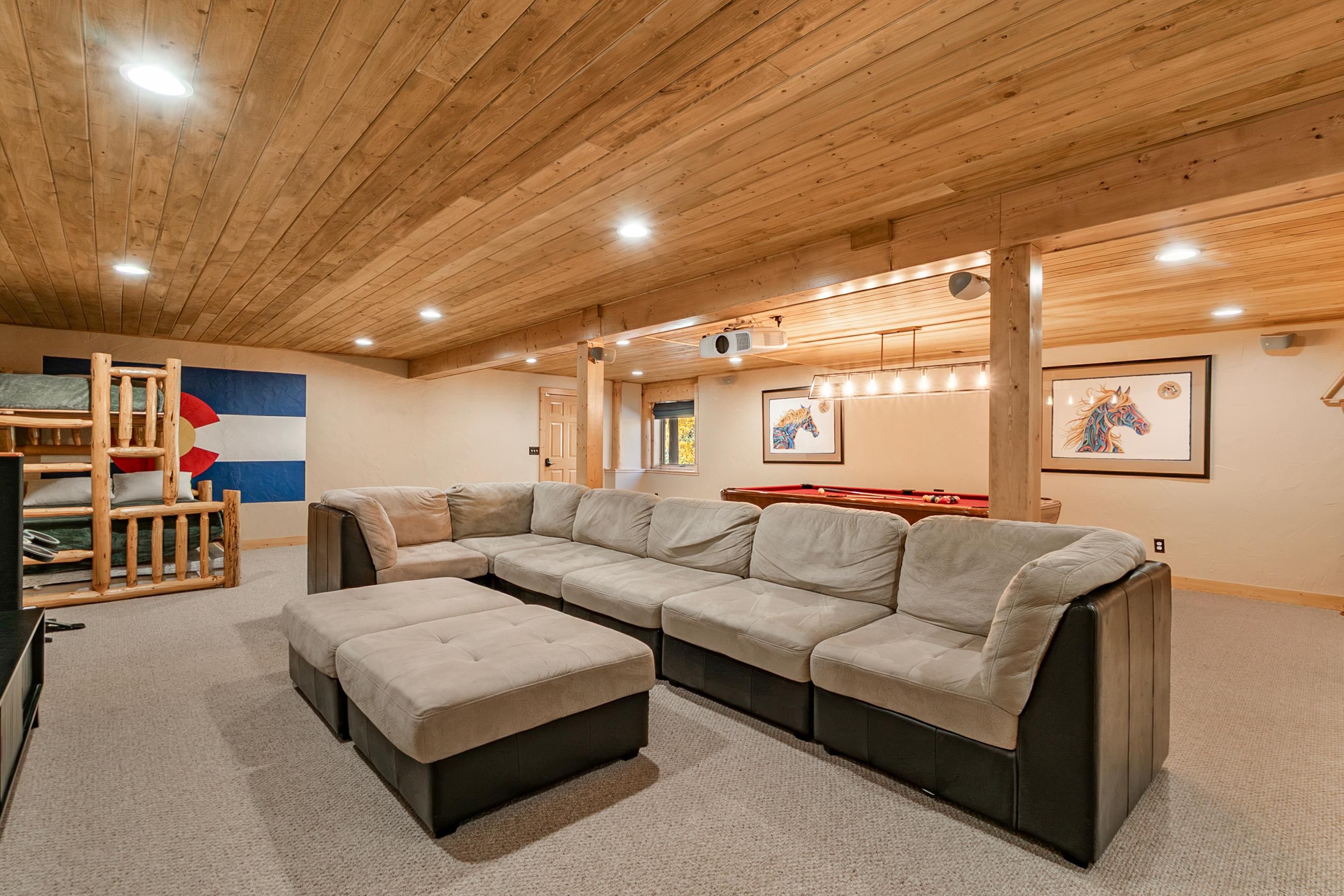 A room with a sectional sofa, a pool table, and a wooden ceiling.