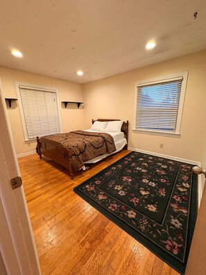 Un dormitorio con una cama de madera, un tapete floral y dos ventanas con persianas.