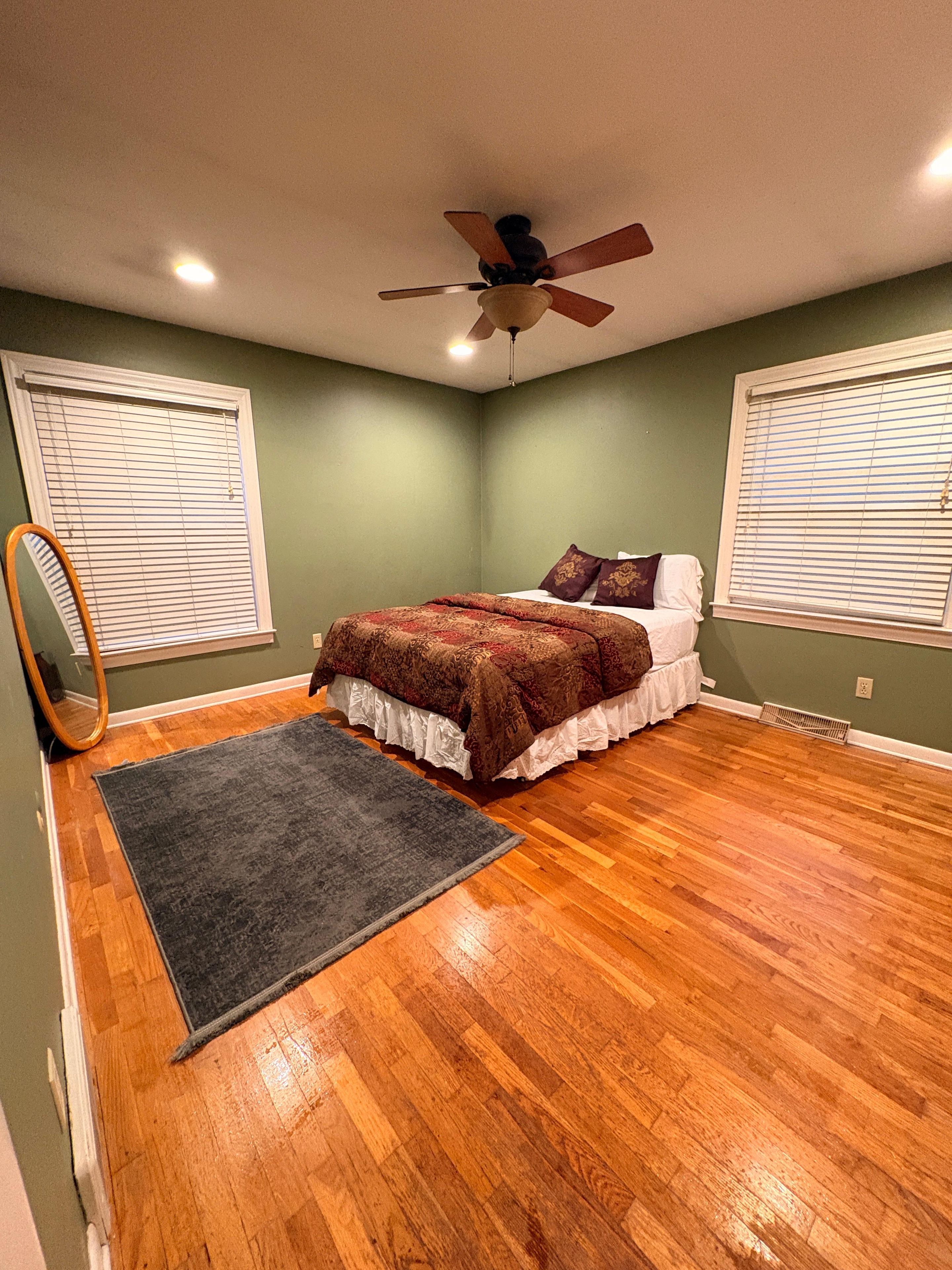 A bedroom with a bed, a ceiling fan, and a wooden floor.