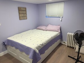 A bedroom with a bed, a wall-mounted sign, a window with blinds, and a radiator. - Junction Gem: Bright, Renovated 1-Bedroom
basement apartment unit with laundry (Toronto)