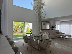 A modern living room with a glass dining table, comfortable seating, a large mirror, and a view of a lush garden. - Luxury New Lisbon/Beach Villa-3 bd, 4 bth, Jacuzzi, Fireplaces, Heated Salt Pool (Setúbal)