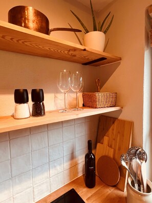 A kitchen with wooden shelves, salt and pepper shakers, wine glasses, a bottle of wine, and kitchen utensils. - Small, cozy, charming—a bright home in Chiemgau (Ruhpolding)