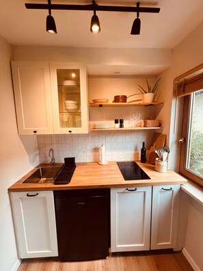 A modern kitchen with a dishwasher, a sink, and a countertop with a kettle. There are cabinets above the countertop and a window to the right. - Small, cozy, charming—a bright home in Chiemgau (Ruhpolding)