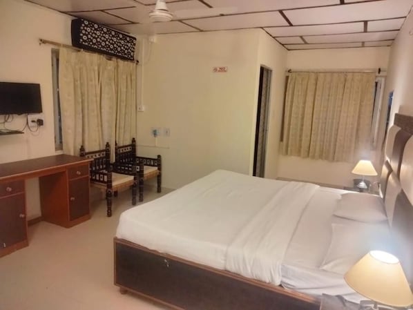 Una habitación de hotel con cama, escritorio, silla, televisor y cortinas.