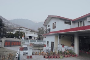 A two-story house with a covered porch, potted plants, and a mountain backdrop.