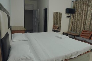Quarto de hotel com cama, televisão, cadeira e mesa pequena.