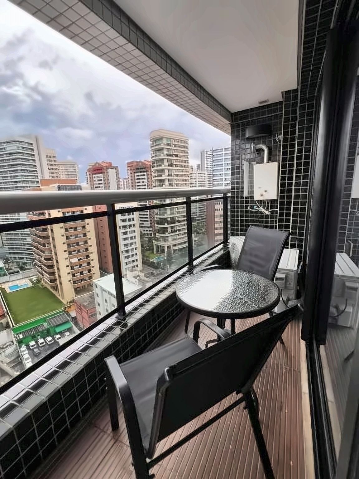 A balcony with a round table and two chairs, a view of a cityscape, and tiled walls.