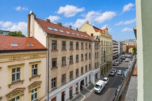 Vista de la calle con edificios de varios pisos, cielo despejado y coches estacionados.
