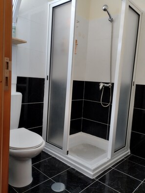 Un baño con inodoro blanco, cabina de ducha con puerta de cristal y paredes con azulejos negros.