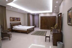 Ein Schlafzimmer mit einem Bett, einem Sessel, einem Schreibtisch, einem Kleiderschrank und einem Bild an der Wand.