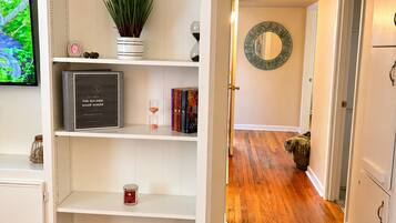 A room with a white built-in shelving unit, a potted plant, a clock, a framed mirror, and a wooden floor.