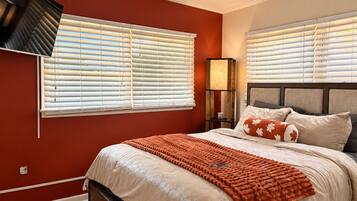 A bedroom with a bed, a nightstand, a lamp, and a wall-mounted TV.