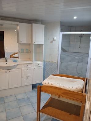 Un baño con lavamanos, espejo, armarios y zona de ducha.