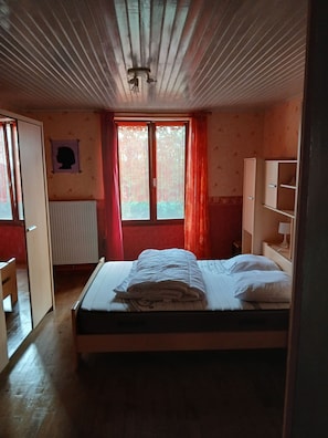 Un dormitorio con cama, radiador, ventana con cortinas, armario y cabecera.