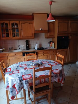 Une cuisine avec des meubles en bois, un pare-feu en carrelage, une table ronde recouverte d’une nappe matelassée et un luminaire suspendu.