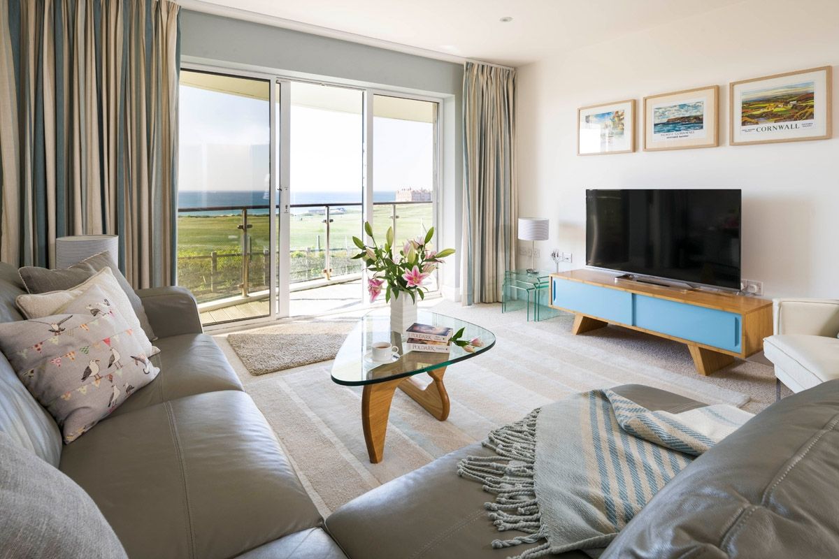 A modern living room with a sofa, a glass coffee table, a flat-screen TV, and a view of the outdoors.
