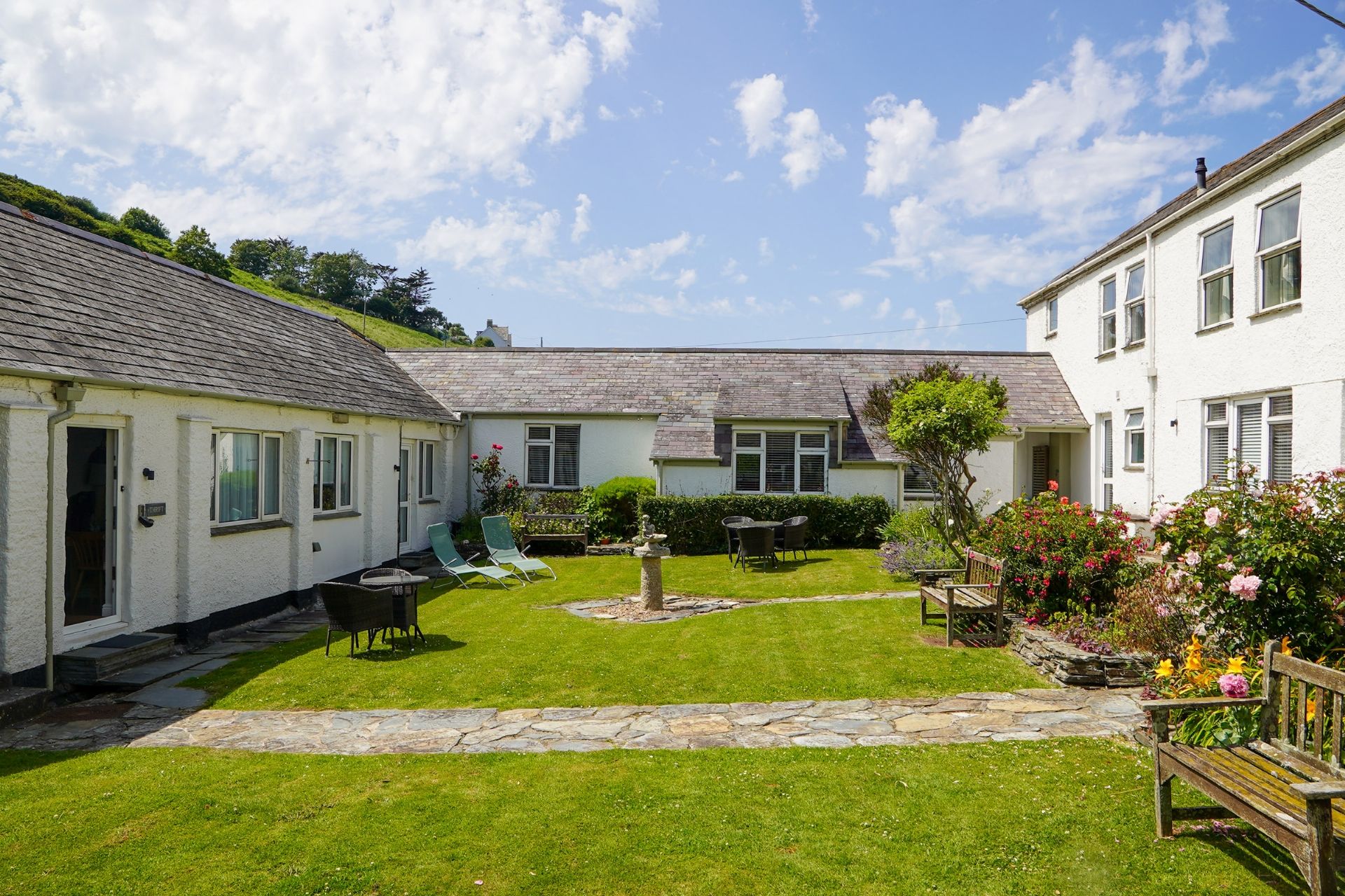 A courtyard with a stone pathway, a grassy lawn, and a seating area with chairs and a table.