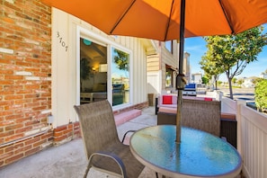 A patio with a glass table and chairs, an orange umbrella, and a brick wall with a number sign. - Short Walk To Sand Prefect For Families, Lrg Patio (Newport Beach)