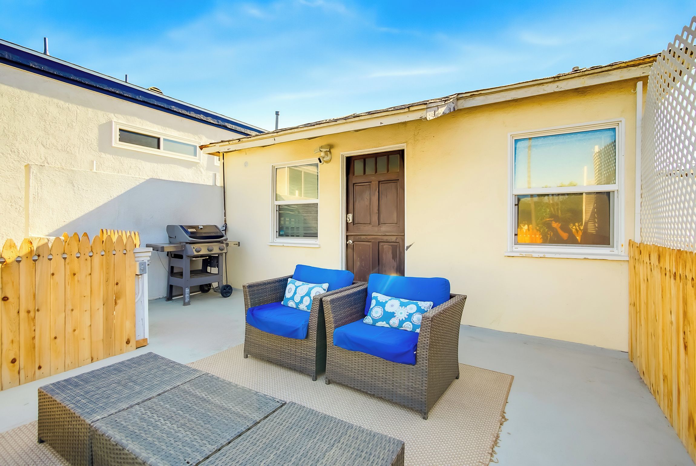 Une terrasse avec deux fauteuils en osier, une petite table et un barbecue.