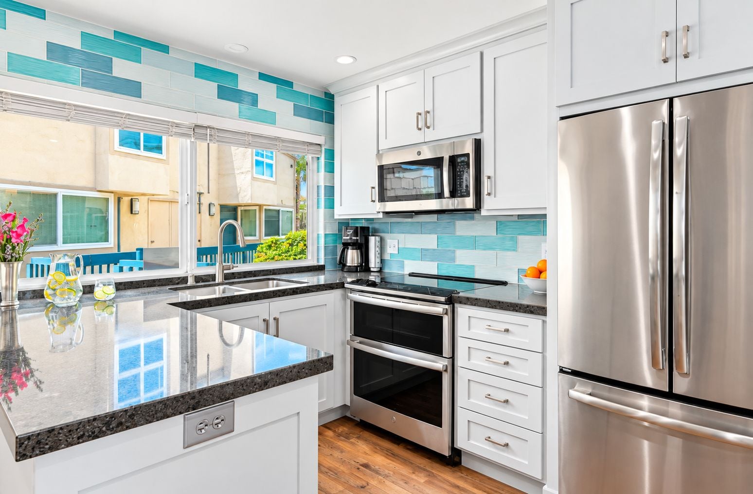 A modern kitchen with stainless steel appliances, white cabinetry, and a teal backsplash.