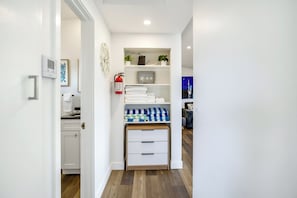 Passadís modern i ben il·luminat amb una porta blanca, una petita cuina i un espai d'emmagatzematge amb tovalloles plegades i un extintor.