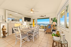 Uma sala de estar ampla com uma mesa de jantar, cadeiras e vista para o oceano.