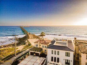 Uma área residencial costeira com um cais que se estende para o mar, um passeio pavimentado e edifícios com varandas.