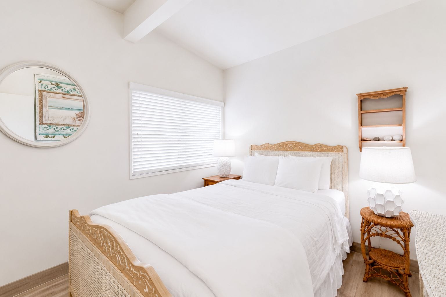 A bedroom with a bed, a nightstand, a lamp, a wall-mounted shelf, and a window with blinds.