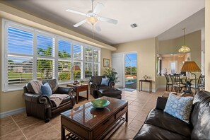 A spacious living room with a large window, a ceiling fan, and a dining area with a view of the outdoors. - Cape Escape your waterfront getaway in SW Cape Coral (Cape Coral)