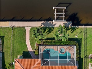 An aerial view of a residential property with a swimming pool, a patio, and a fenced area with palm trees. - Cape Escape your waterfront getaway in SW Cape Coral (Cape Coral)