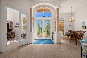 A spacious foyer with a double door, a dining area with a chandelier, and a view of the outdoors. - Cape Escape your waterfront getaway in SW Cape Coral (Cape Coral)