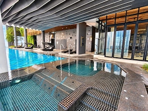 An indoor swimming pool with a tiled floor, lounge chairs, and a modern architectural design. - Scarletz KLCC By Solvane Hospitality  (Kuala Lumpur)