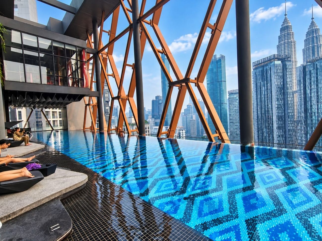 Una piscina infinita con un patrón geométrico de azulejos, rodeada por una estructura moderna y vistas al horizonte de la ciudad.