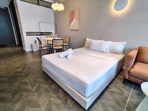 A hotel room with a large bed, a desk with chairs, a small table with bottles, and a wall-mounted light fixture. - Scarletz KLCC By Solvane Hospitality  (Kuala Lumpur)